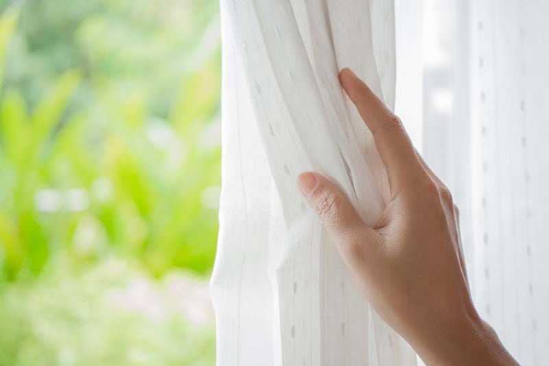 Image of someone pulling back curtains on window. Spring Money-Saving Tips.