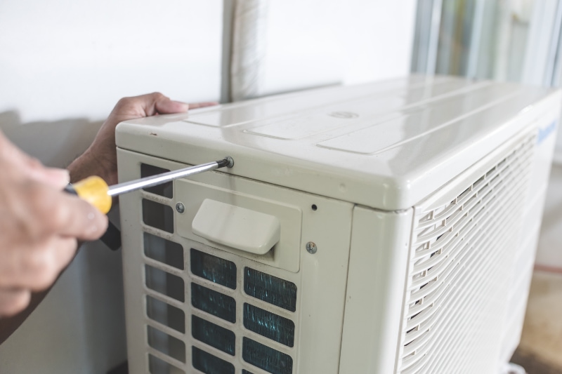 A technician unscrews the top hatch of the outdoor compressor unit of a Split type air conditioner. Repair or maintenance work.