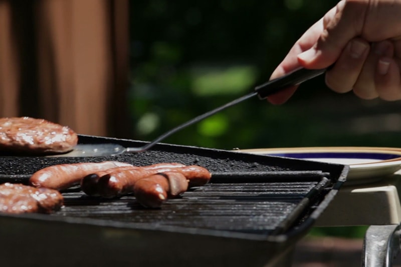 Video - Energy Saving Tip 1. Grill with hot dogs on it and hand with spatula turning them.