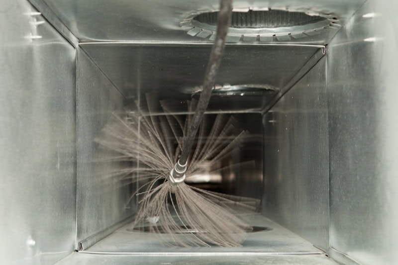Breathe Easy This Holiday Season: Why Duct Cleaning Matters. Photo of a cleaning brush inside air ducts.