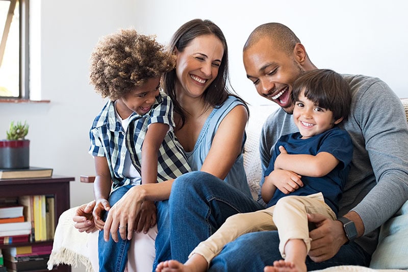 How Do Air Purifiers and Air Filters Work? Photo of a family of four laughing and spending time together on a couch.