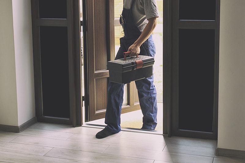 7 Furnace Maintenance Tips to Stay Cozy. Maintenance technician walking in home with toolbox.